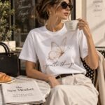 Woman at a cafe table wearing the Gentle Things butterfly t-shirt - sepia butterfly tee GTA