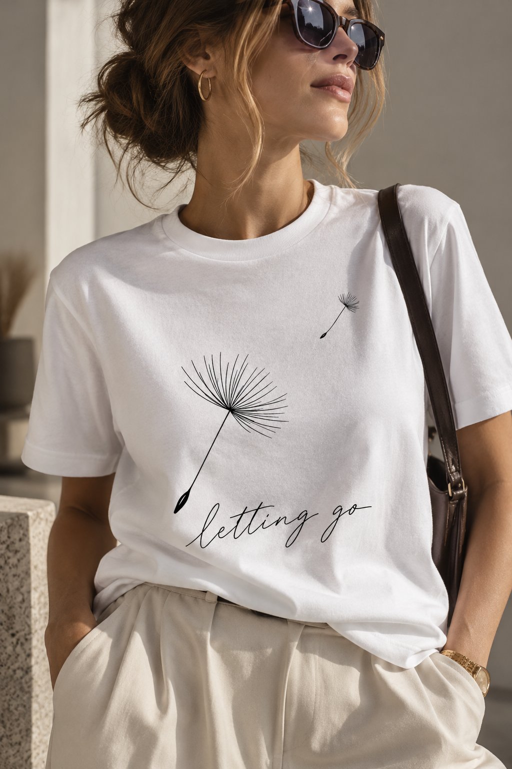 Woman wearing the Letting Go dandelion t-shirt with a shoulder bag - minimalist line art tee - PrintMyVibe Toronto